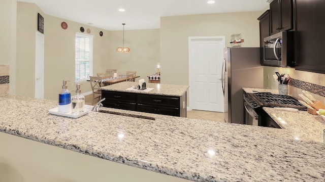 kitchen featuring appliances with stainless steel finishes, a sink, light stone counters, and a center island