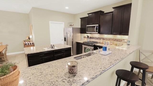 kitchen featuring light stone counters, a breakfast bar, stainless steel appliances, decorative backsplash, and a sink