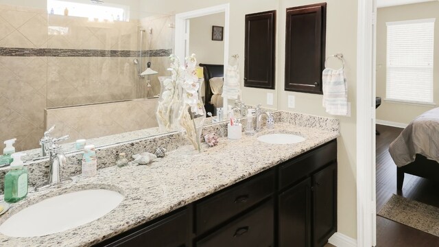 bathroom featuring wood finished floors, double vanity, a sink, and a walk in shower