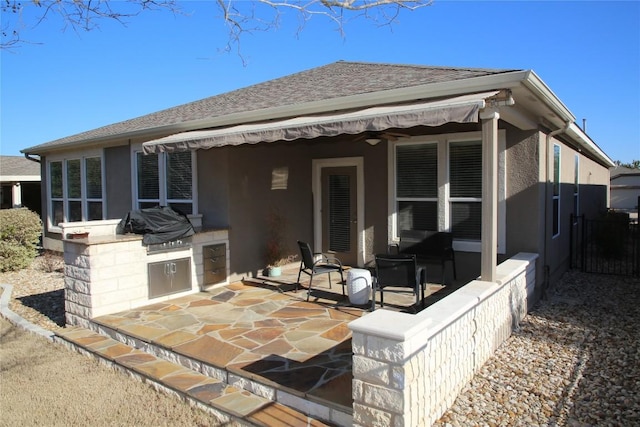 rear view of house with a patio, a shingled roof, area for grilling, and stucco siding