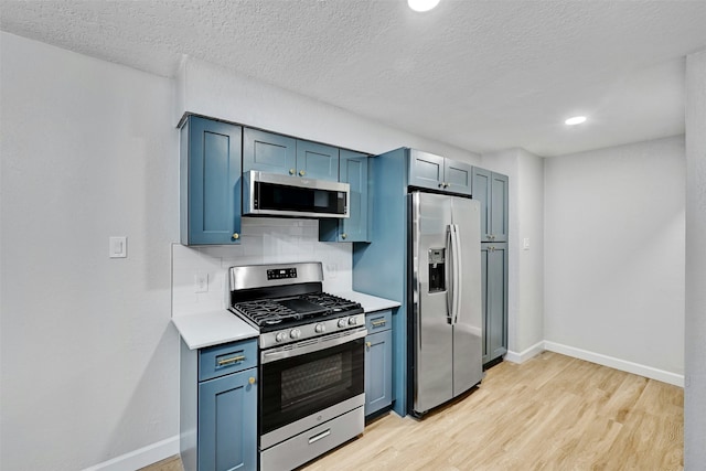 kitchen featuring appliances with stainless steel finishes, blue cabinets, a textured ceiling, light hardwood / wood-style floors, and decorative backsplash