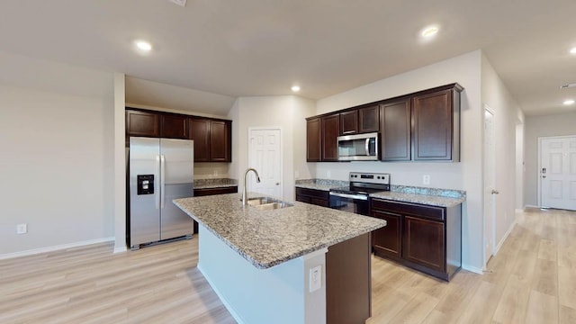 kitchen with light hardwood / wood-style floors, appliances with stainless steel finishes, a kitchen island with sink, sink, and light stone counters