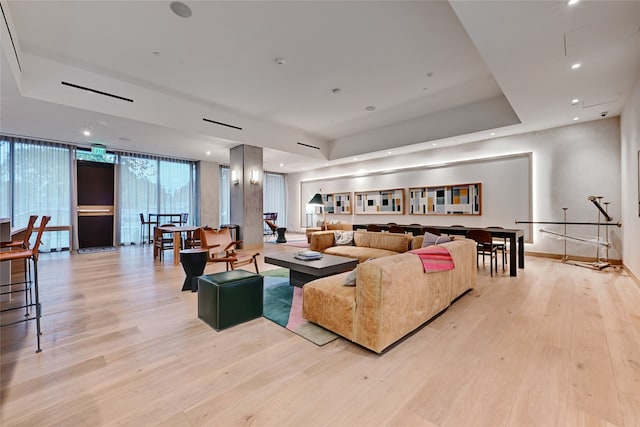 living room with light hardwood / wood-style floors, a wall of windows, and a raised ceiling