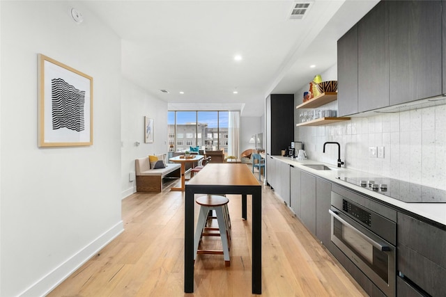 kitchen with stainless steel oven, decorative backsplash, black electric cooktop, sink, and light hardwood / wood-style flooring