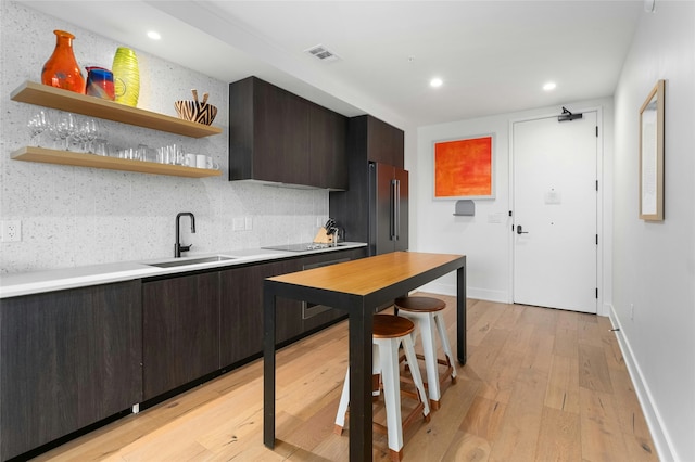 kitchen with high quality fridge, tasteful backsplash, sink, dark brown cabinetry, and light hardwood / wood-style flooring