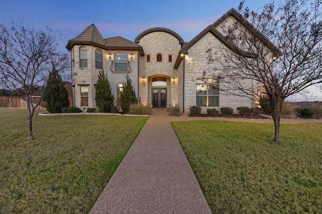 french country home with a balcony, a lawn, and french doors