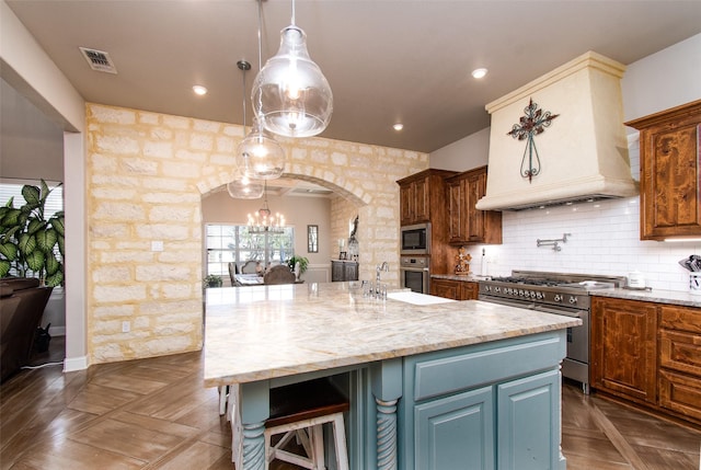 kitchen featuring dark parquet flooring, decorative light fixtures, stainless steel appliances, an island with sink, and gray cabinetry