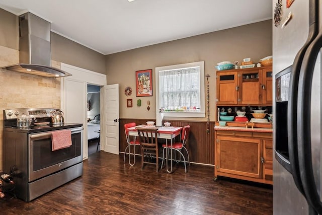 kitchen featuring wall chimney range hood, wood walls, appliances with stainless steel finishes, and dark wood-type flooring