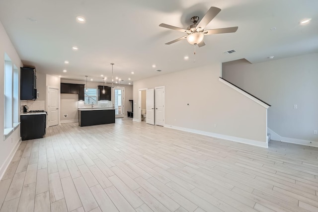 unfurnished living room featuring light wood-type flooring and ceiling fan with notable chandelier