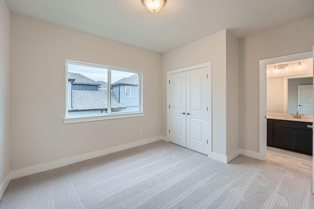 unfurnished bedroom with light carpet, a closet, sink, and connected bathroom