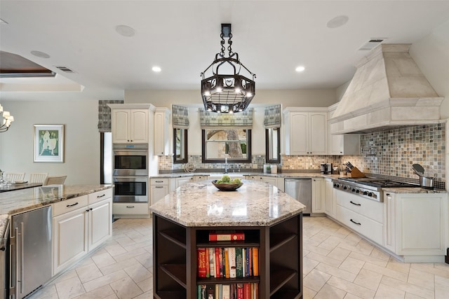 kitchen featuring hanging light fixtures, custom range hood, white cabinetry, light stone countertops, and a kitchen island