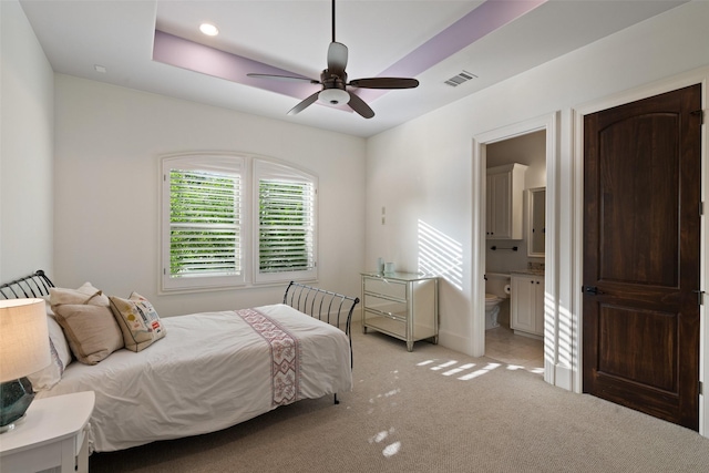 bedroom featuring ceiling fan, light carpet, a tray ceiling, and ensuite bathroom