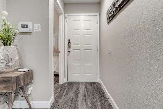 doorway featuring wood finished floors, baseboards, and a textured wall