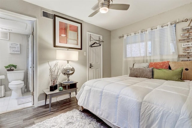 bedroom with a ceiling fan, baseboards, wood finished floors, visible vents, and connected bathroom