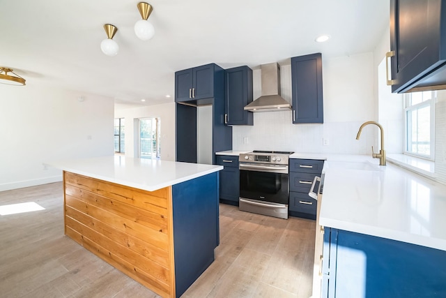 kitchen with wall chimney range hood, light hardwood / wood-style floors, electric stove, blue cabinetry, and sink