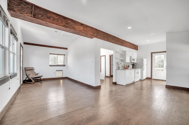 unfurnished living room with wood-type flooring, lofted ceiling with beams, and a healthy amount of sunlight