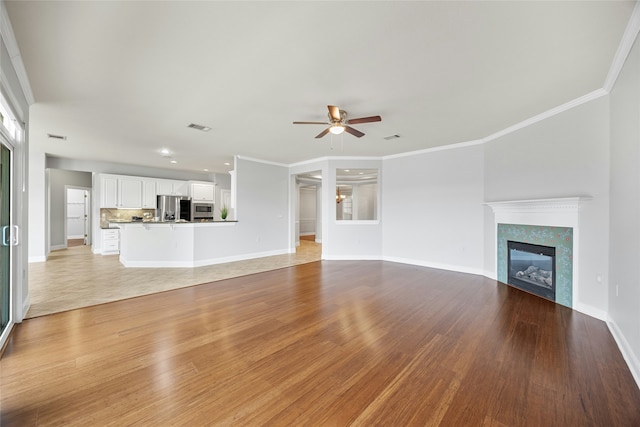 unfurnished living room with a fireplace, light hardwood / wood-style flooring, ceiling fan, and crown molding