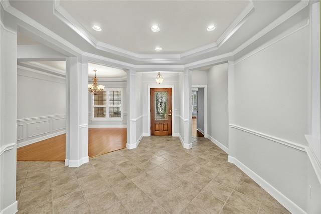 foyer entrance with a tray ceiling, ornamental molding, and a notable chandelier