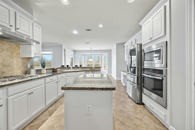 kitchen featuring white cabinets, appliances with stainless steel finishes, a center island, and dark stone countertops