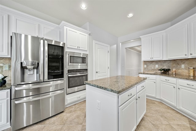 kitchen with white cabinets, a center island, stainless steel appliances, dark stone counters, and tasteful backsplash