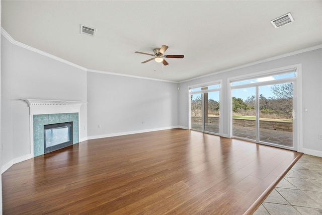 unfurnished living room with ceiling fan, ornamental molding, light hardwood / wood-style floors, and a tiled fireplace