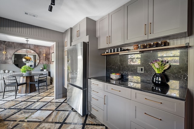 kitchen featuring gray cabinetry, dark stone countertops, pendant lighting, backsplash, and stainless steel fridge