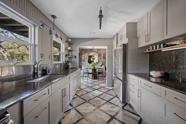 kitchen with pendant lighting, stainless steel fridge, sink, backsplash, and dark stone countertops