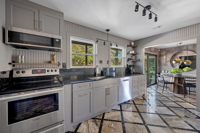 kitchen featuring white cabinets, appliances with stainless steel finishes, decorative light fixtures, dark stone countertops, and sink