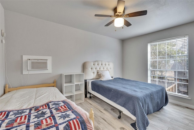 bedroom featuring a wall mounted AC, light hardwood / wood-style flooring, and ceiling fan