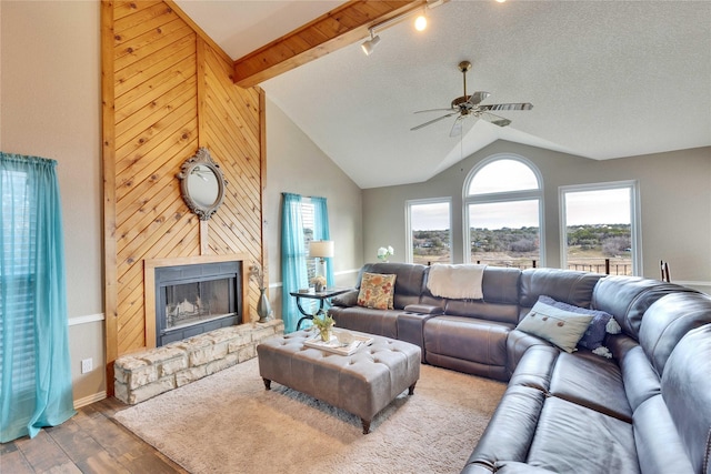 living room with a stone fireplace, vaulted ceiling with beams, dark hardwood / wood-style floors, wood walls, and ceiling fan