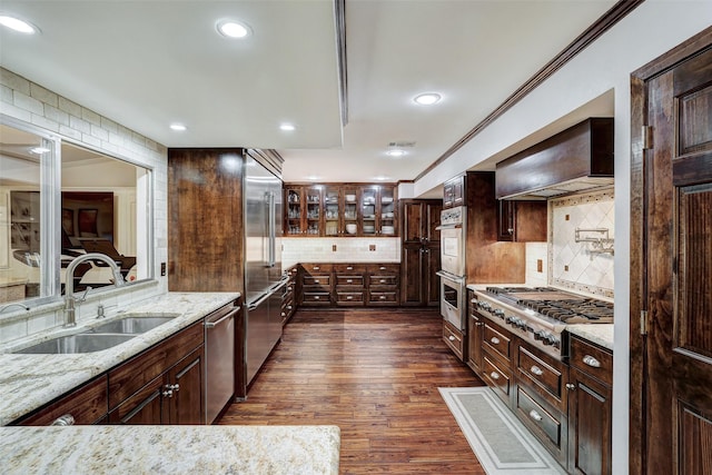 kitchen featuring appliances with stainless steel finishes, sink, premium range hood, tasteful backsplash, and light stone countertops