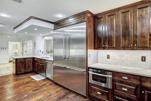 kitchen with appliances with stainless steel finishes, decorative backsplash, sink, dark hardwood / wood-style flooring, and light stone counters