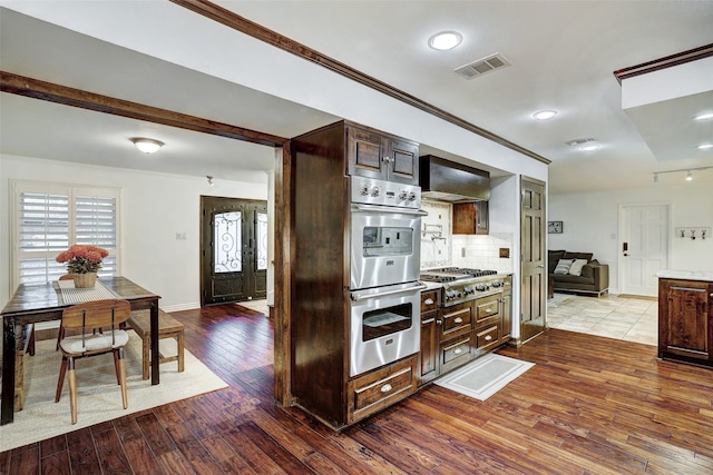 kitchen featuring tasteful backsplash, wall chimney range hood, dark brown cabinetry, light hardwood / wood-style flooring, and stainless steel appliances