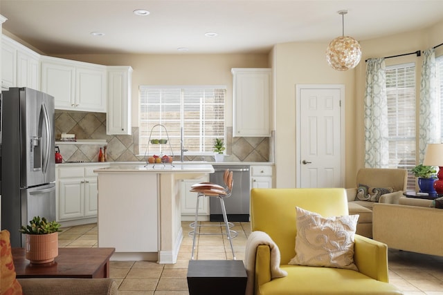 kitchen with a kitchen island, decorative light fixtures, stainless steel appliances, white cabinets, and tasteful backsplash