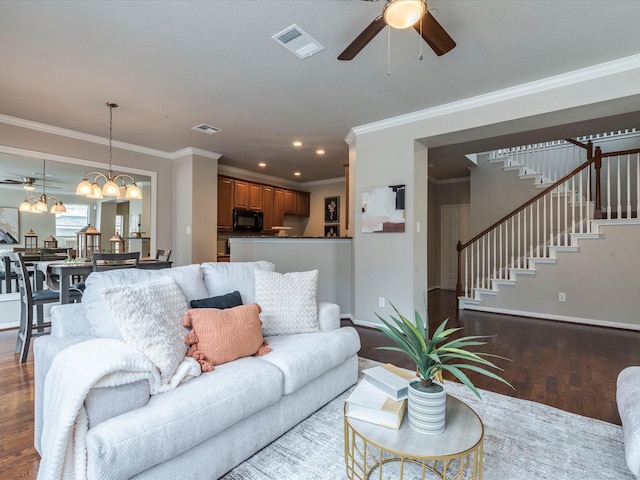 living room featuring dark wood-type flooring, ceiling fan with notable chandelier, and ornamental molding