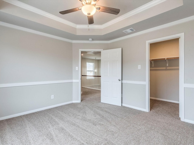 unfurnished bedroom with carpet, a walk in closet, a closet, ceiling fan, and crown molding