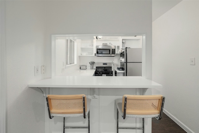 kitchen with a kitchen breakfast bar, appliances with stainless steel finishes, dark hardwood / wood-style floors, and kitchen peninsula