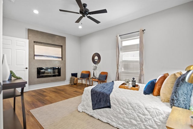 bedroom with ceiling fan, dark wood-type flooring, and a fireplace