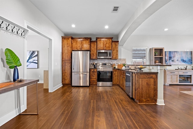 kitchen featuring sink, backsplash, dark hardwood / wood-style floors, dark stone countertops, and stainless steel appliances