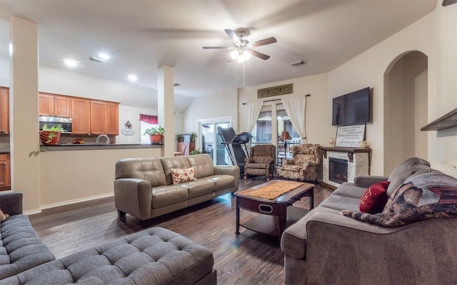 living room featuring sink, a stone fireplace, dark wood-type flooring, and ceiling fan