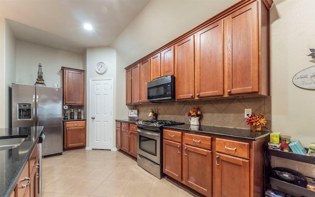 kitchen featuring appliances with stainless steel finishes, lofted ceiling, backsplash, dark stone counters, and light tile patterned floors