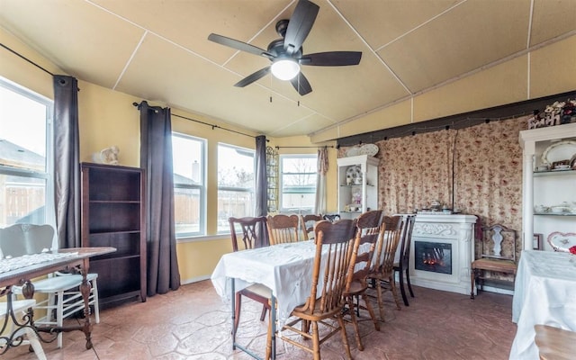 dining area with vaulted ceiling, ceiling fan, and a glass covered fireplace