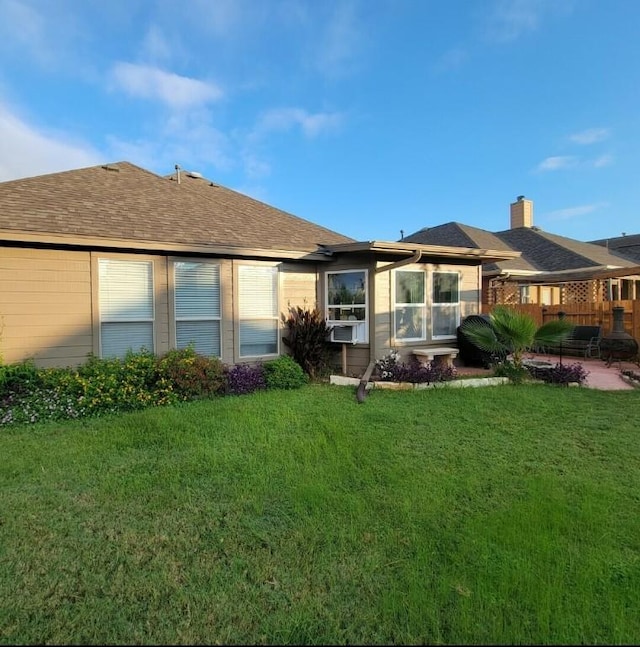 rear view of property featuring a patio, a shingled roof, a lawn, and cooling unit