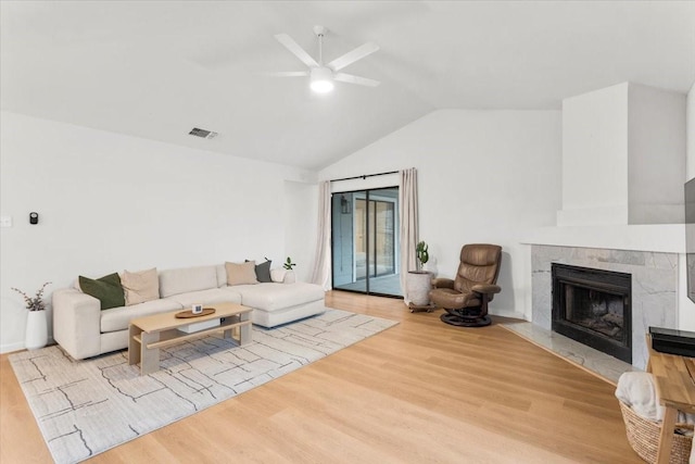 living room with ceiling fan, a high end fireplace, light hardwood / wood-style flooring, and lofted ceiling