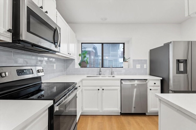 kitchen with white cabinets, appliances with stainless steel finishes, tasteful backsplash, sink, and light hardwood / wood-style flooring