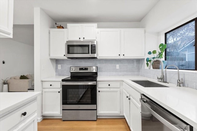 kitchen featuring tasteful backsplash, sink, white cabinets, light hardwood / wood-style flooring, and stainless steel appliances