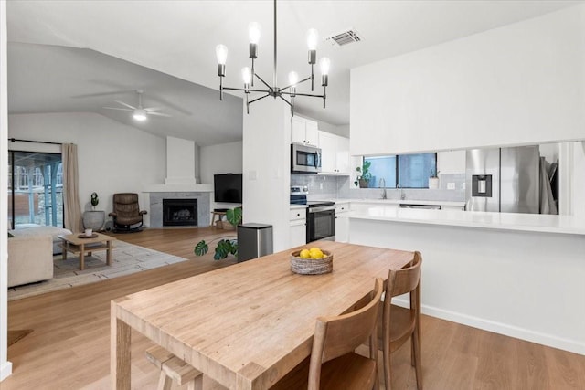 dining space featuring ceiling fan with notable chandelier, sink, lofted ceiling, and light wood-type flooring