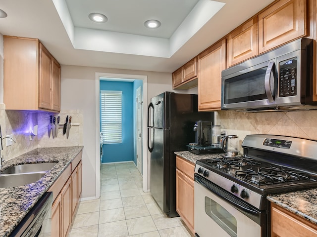 kitchen with appliances with stainless steel finishes, sink, a raised ceiling, dark stone counters, and light tile patterned flooring