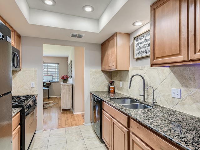 kitchen featuring black appliances, sink, dark stone countertops, a raised ceiling, and light tile patterned flooring