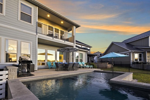 back house at dusk featuring a fenced in pool, a balcony, and a patio area